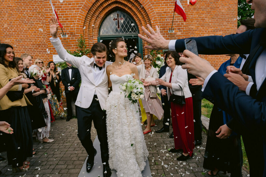 Reporterska fotografia ślubna - WhiteSmoke Studio 29 Natalia i Bartosz wychodzą z kościoła wśród gości